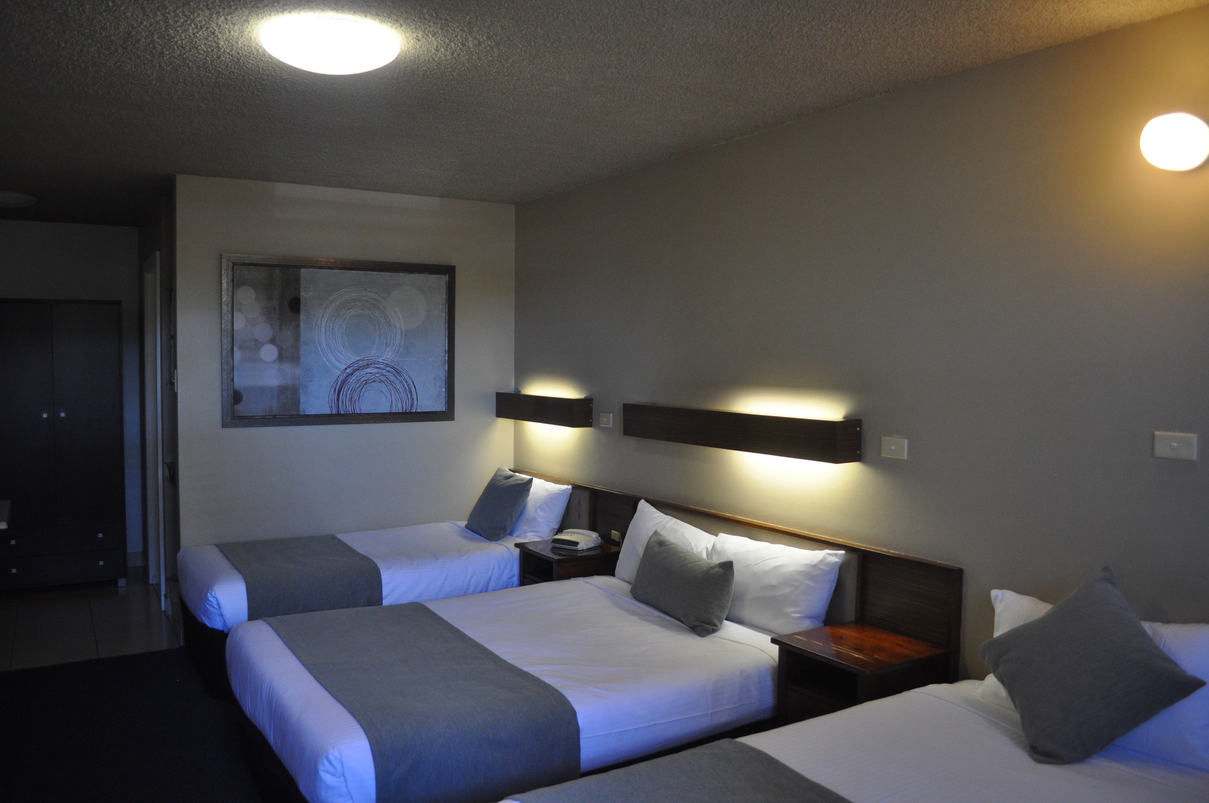 Ein Hotelzimmer mit zwei Betten, jeweils mit einem hölzernen Kopfteil, Nachttischen und einem an der Wand hängenden Kunstwerk.
