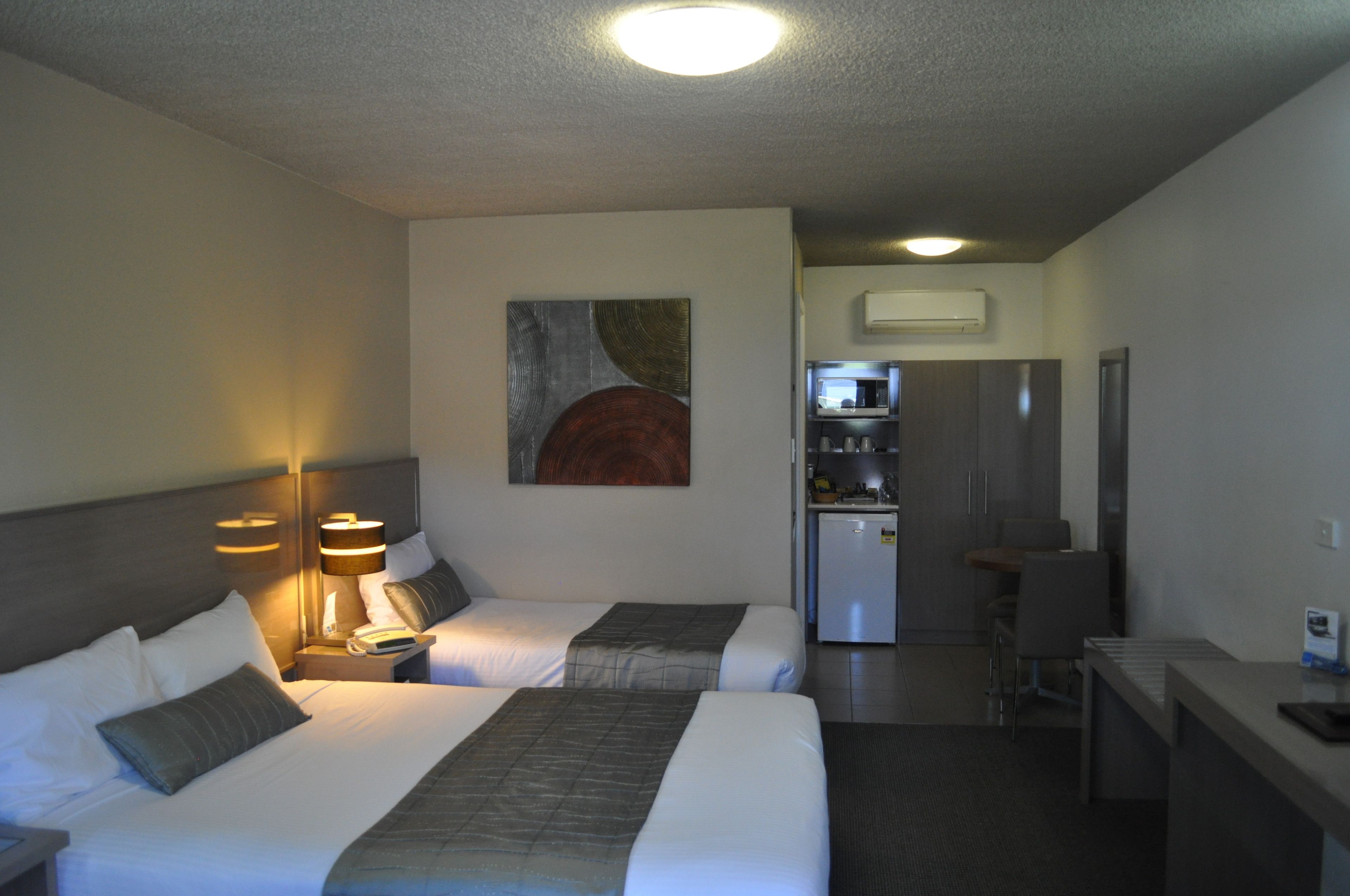 Habitación de hotel con dos camas, un escritorio, una silla, una kitchenette y un cuadro en la pared.