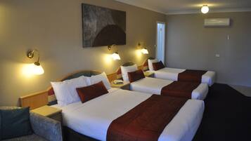 Habitación de hotel con tres camas, cada una con ropa blanca y cabeceras marrones. Dos lámparas de pared a cada lado de las camas.