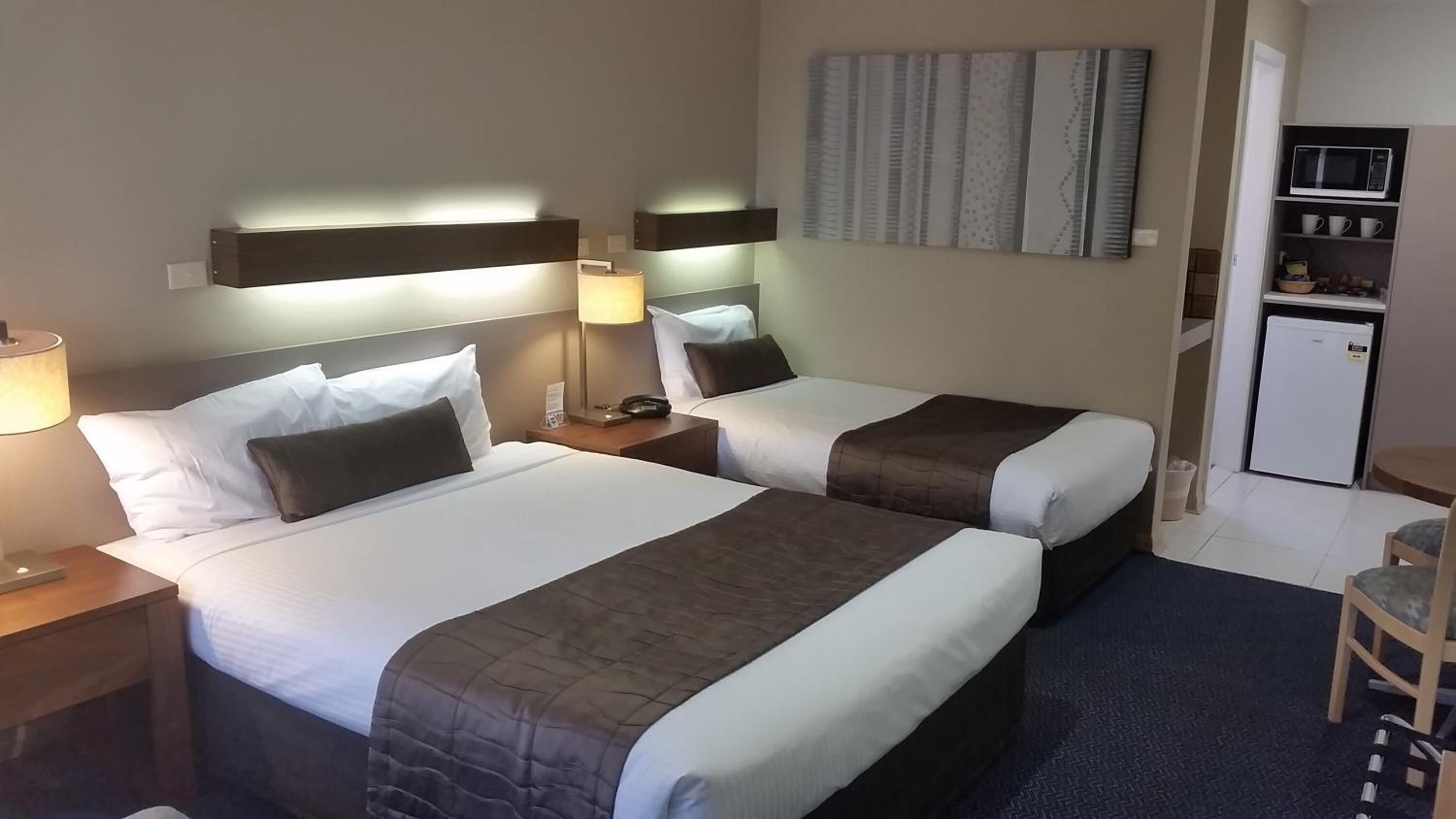 Habitación de hotel con dos camas, lámparas de noche, una mesita, microondas y refrigerador.