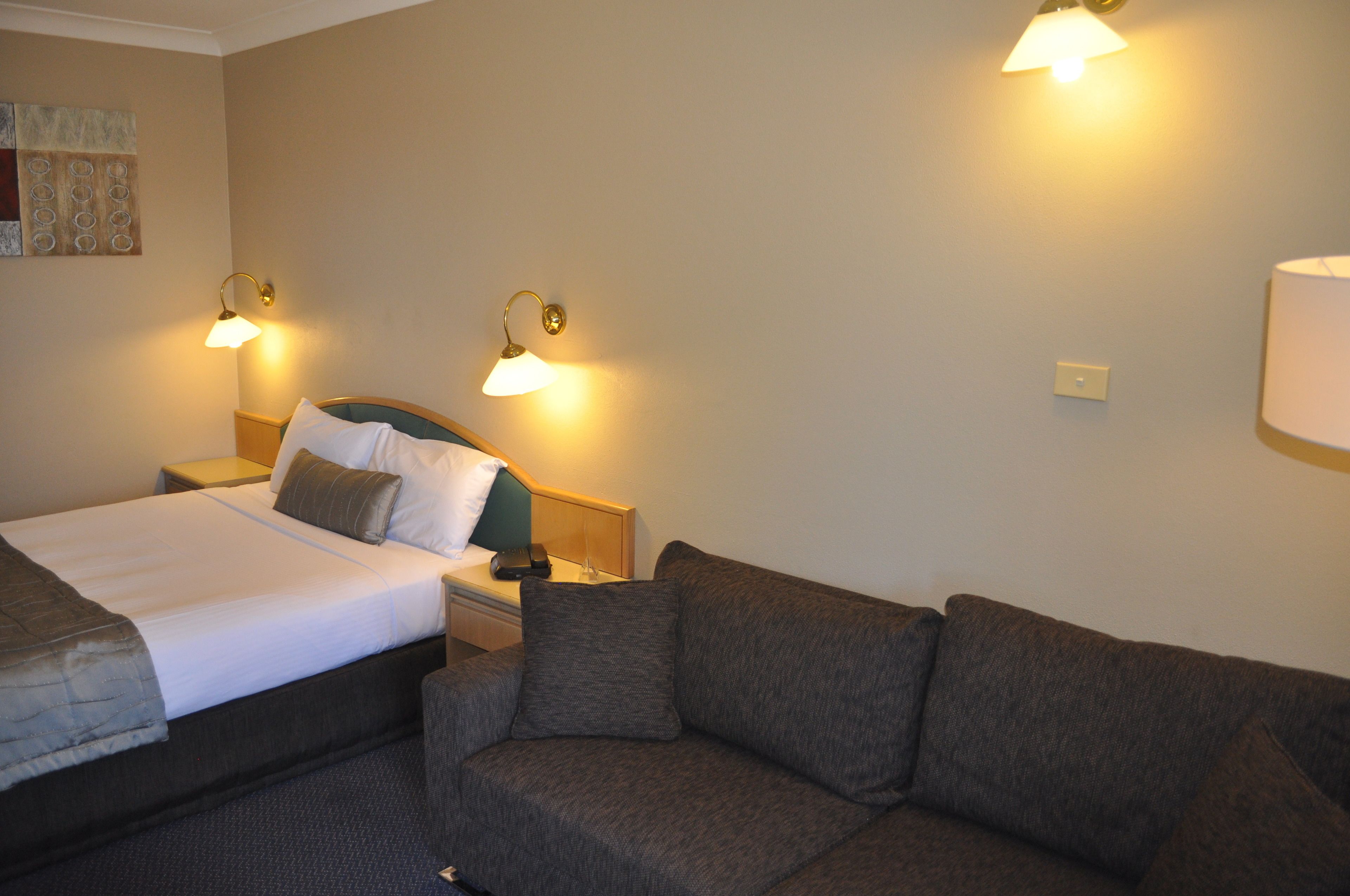 Una habitación de hotel con una cama, un sofá y dos lámparas fijadas a la pared.