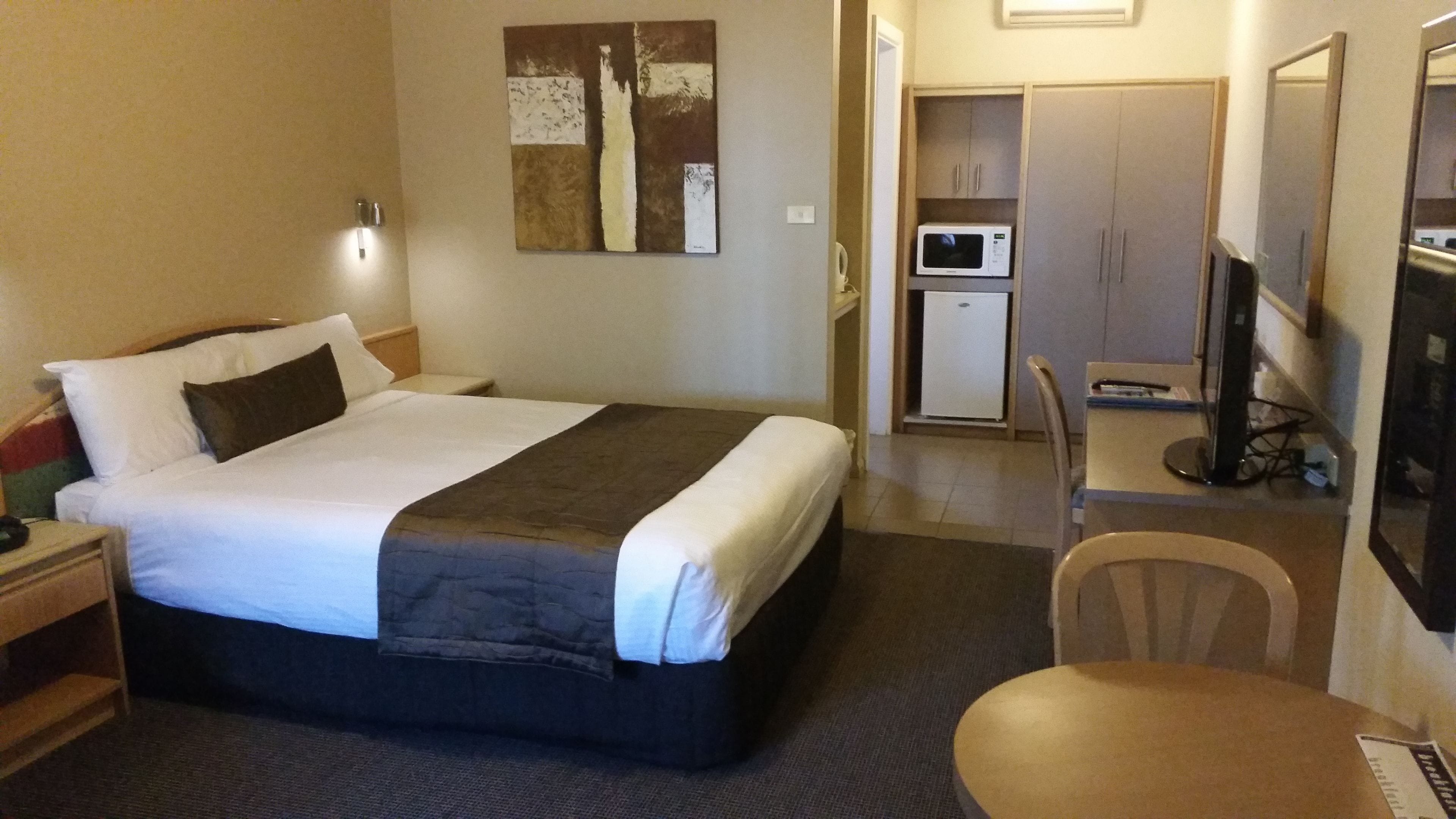 A hotel room with a bed, a desk, a chair, a microwave, and a television.