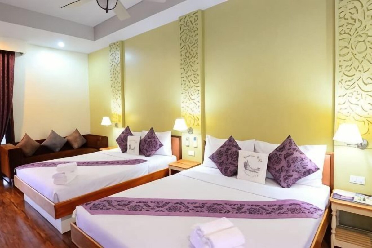 Una habitación de hotel con dos camas, cada una con un almohadón, una mesita de noche con una lámpara y una pared decorada con un diseño ornamental.