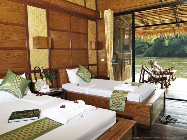 A hotel room with two beds, wooden headboards, a large window with a view of a river, and a wooden deck outside. - Boutique Raft Resort (Sai Yok)