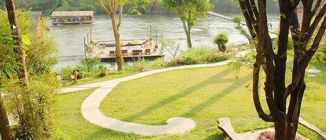 A landscaped garden with a curved pathway, a dock with a boat, and a river in the background.