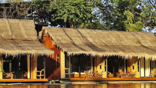 Ett traditionellt hus med halmtak, trämöbler och en spegelbild i vattnet.