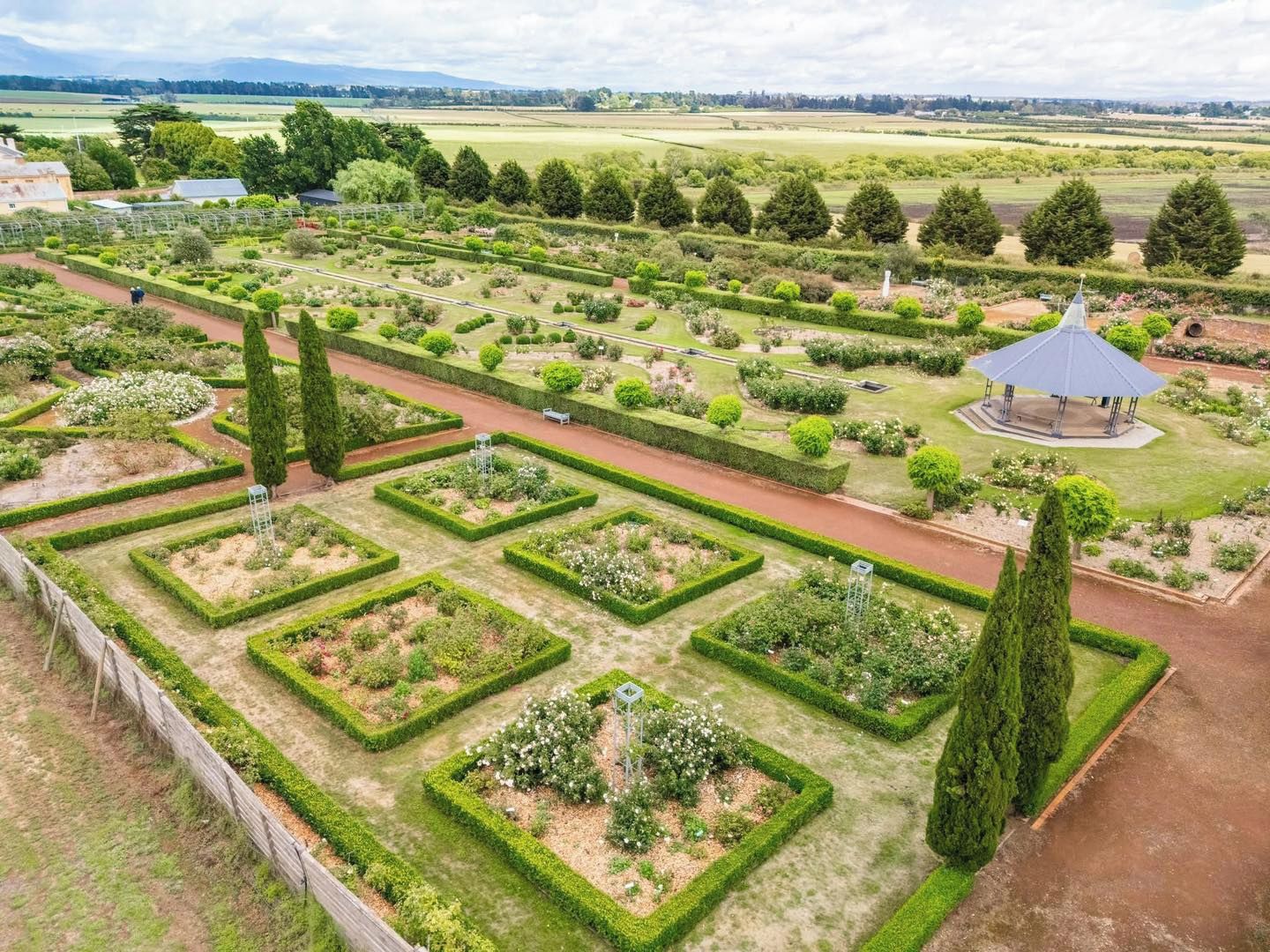 A formal garden with geometric hedges, a central walkway, and a gazebo.