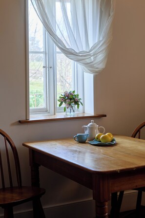 A dining table with a pitcher, cups, and lemons by a window with sheer curtains.