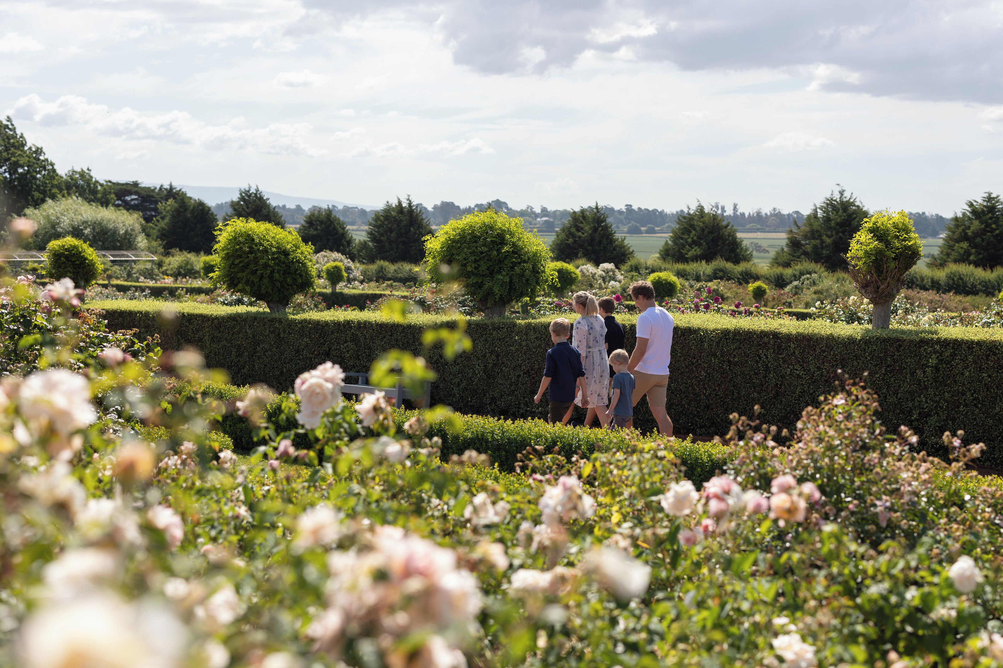 A family walking through a well-manicured garden with hedges and flowering plants.