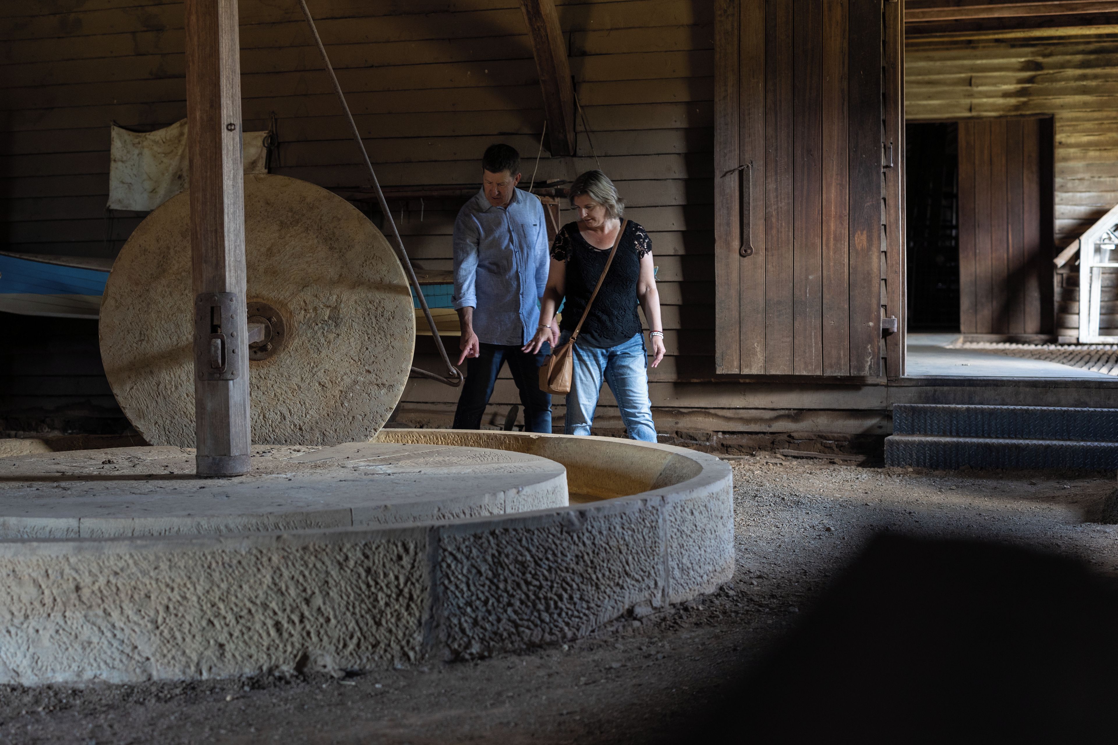 Un interior rústico con una gran estructura circular de piedra, vigas de madera y una puerta que da a un espacio exterior.