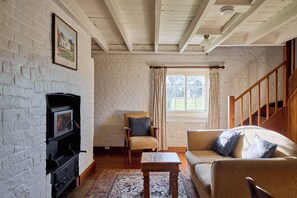 A cozy living room with a fireplace, a sofa, a chair, and a window with curtains. - Woolmers Estate (Longford)
