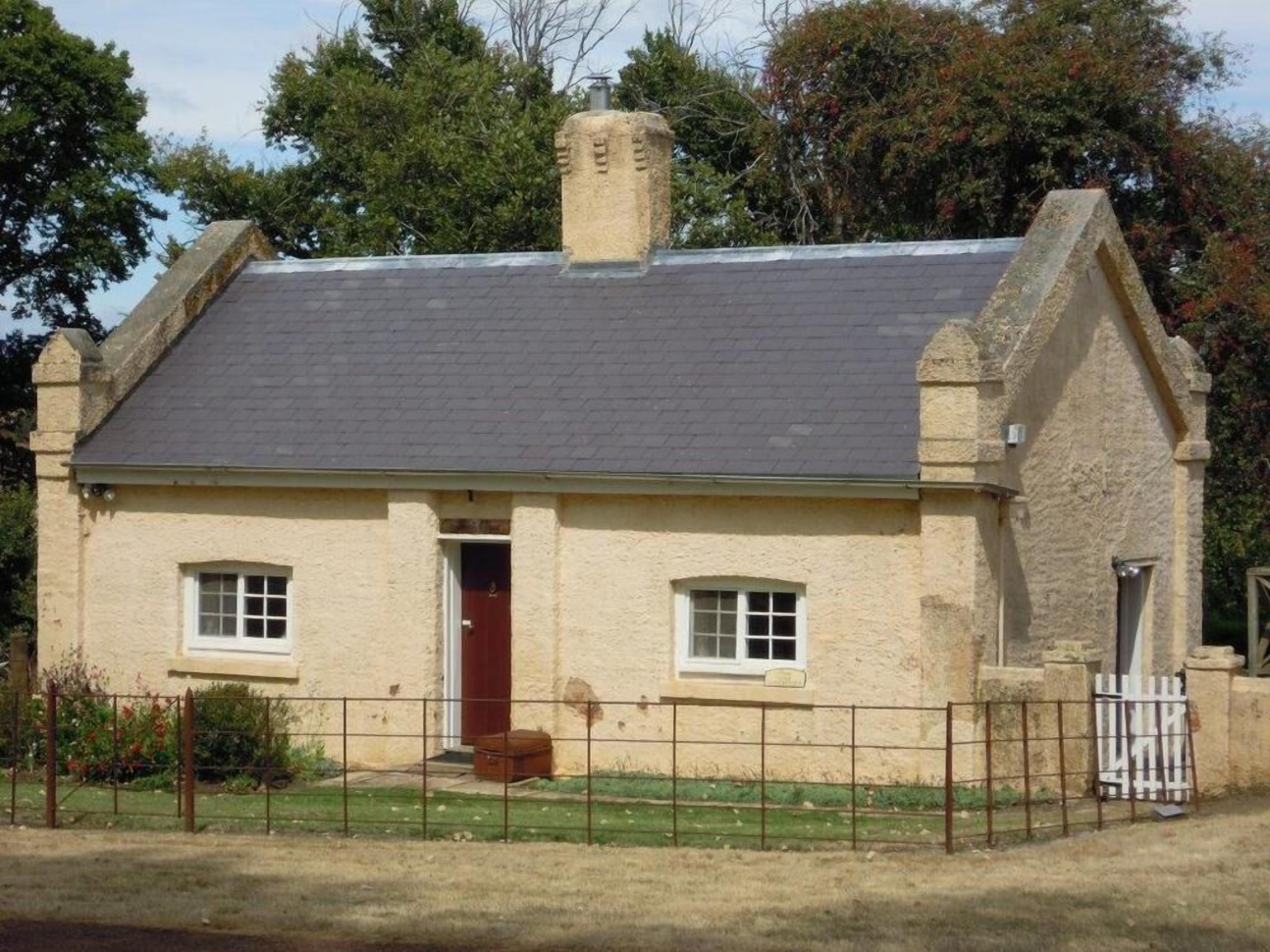 Una pequeña casa de piedra con techo inclinado, dos ventanas y una chimenea.
