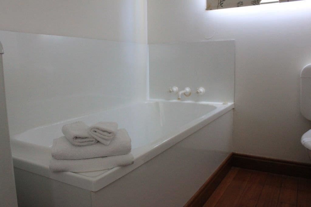 A bathroom with a white bathtub, a toilet, and a window with blinds.