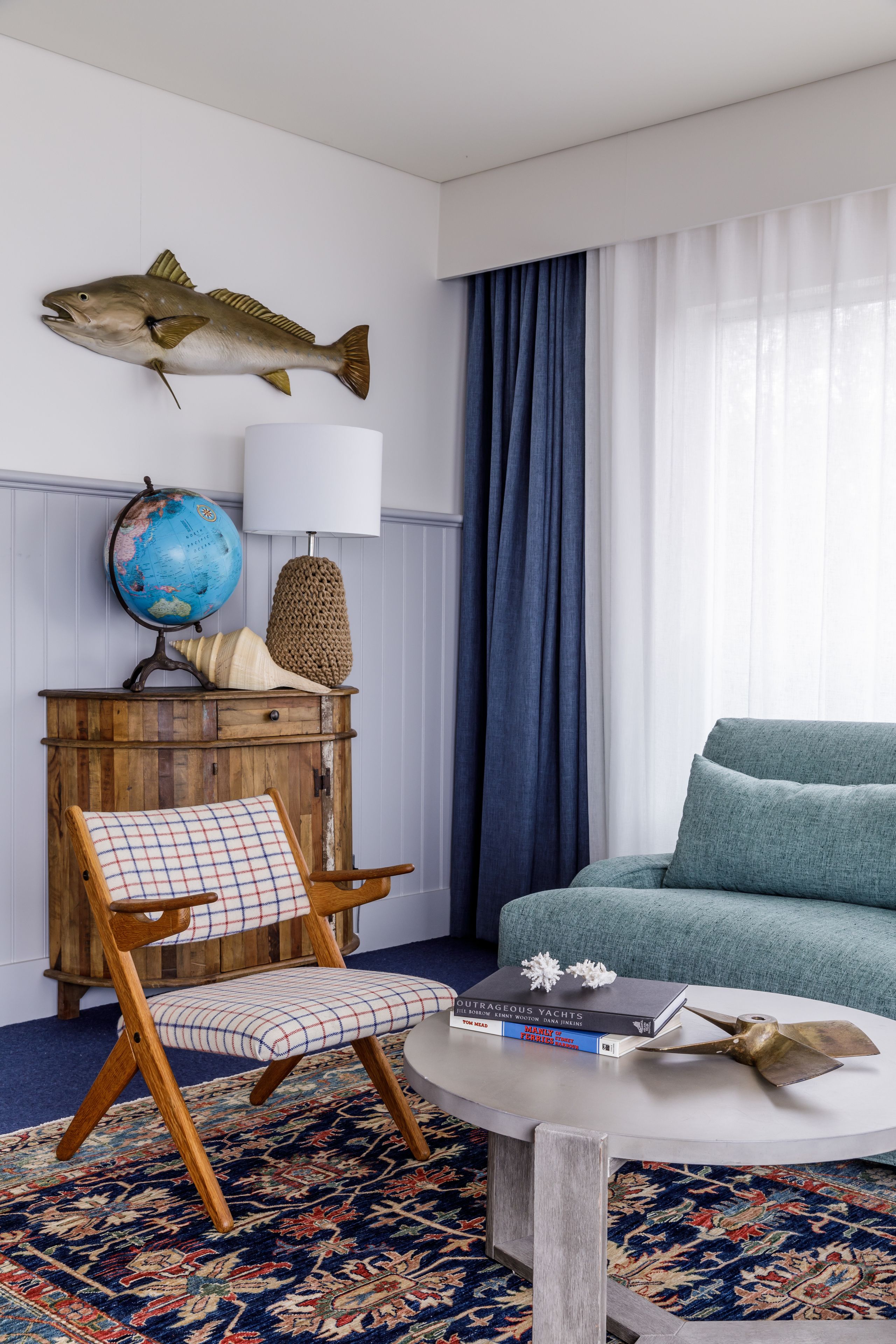 A room with a wooden chair, a globe, a fish wall decoration, a blue sofa, and a patterned rug.