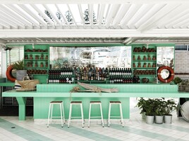 A bar area with green walls, a variety of bottles, and stools.