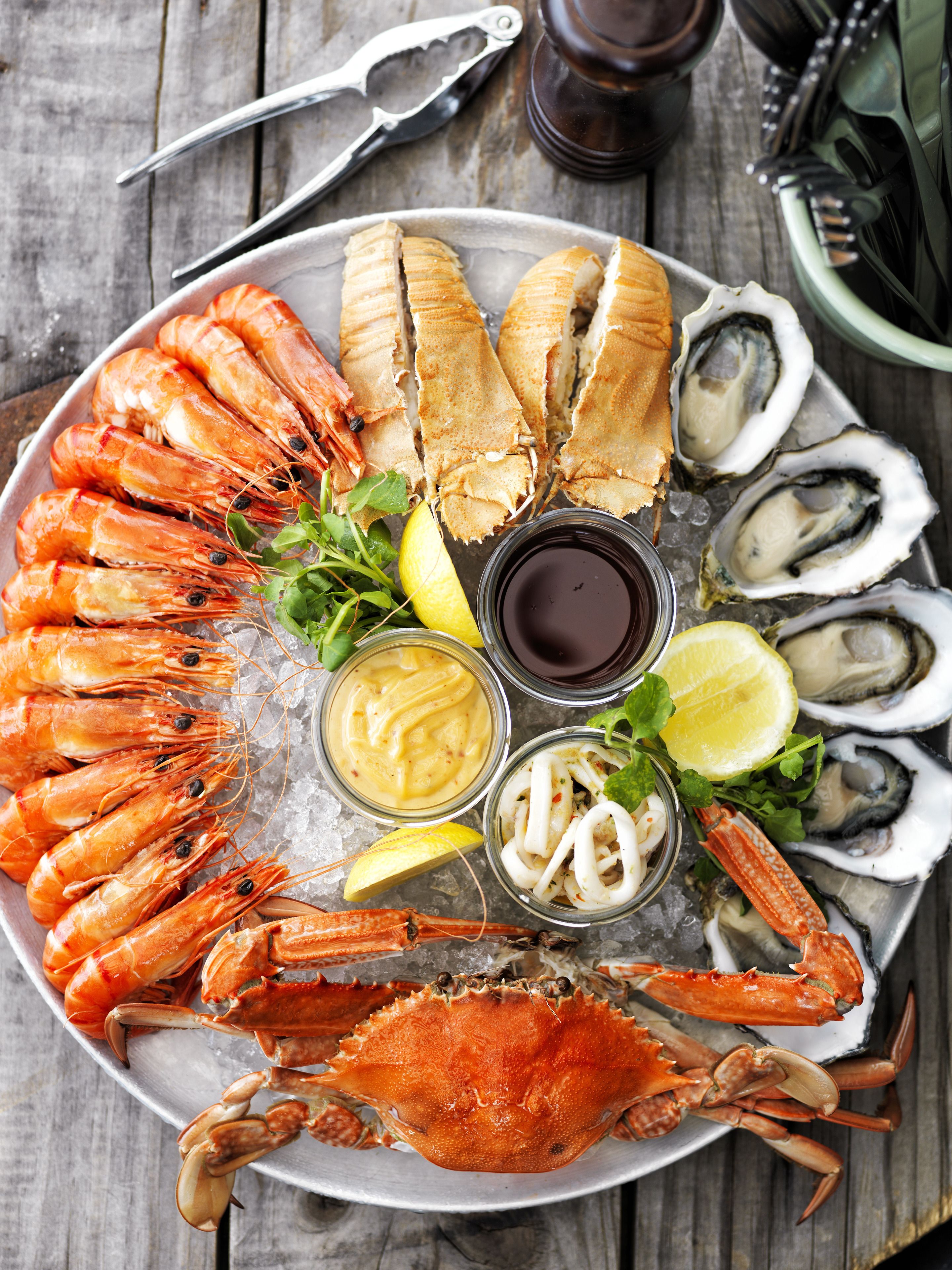 A seafood platter with shrimp, crab, oysters, and lemon slices on a wooden table.
