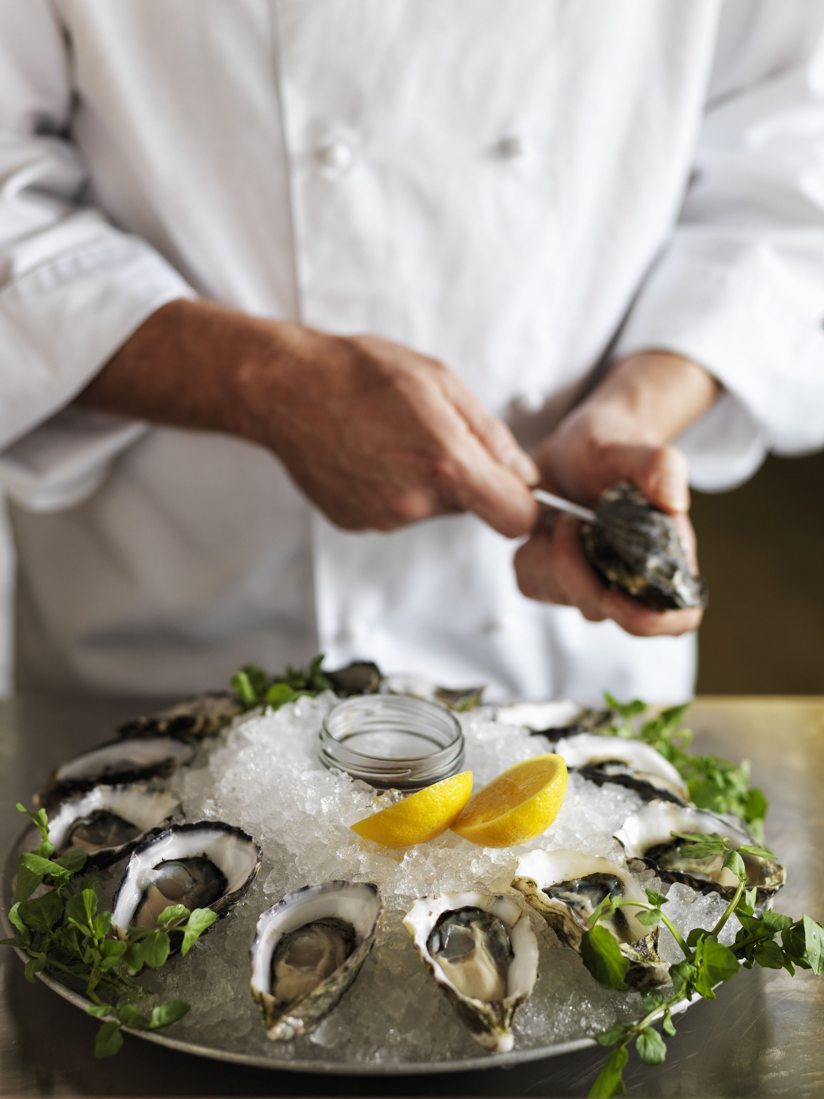A chef preparing oysters on ice with lemon wedges and herbs.