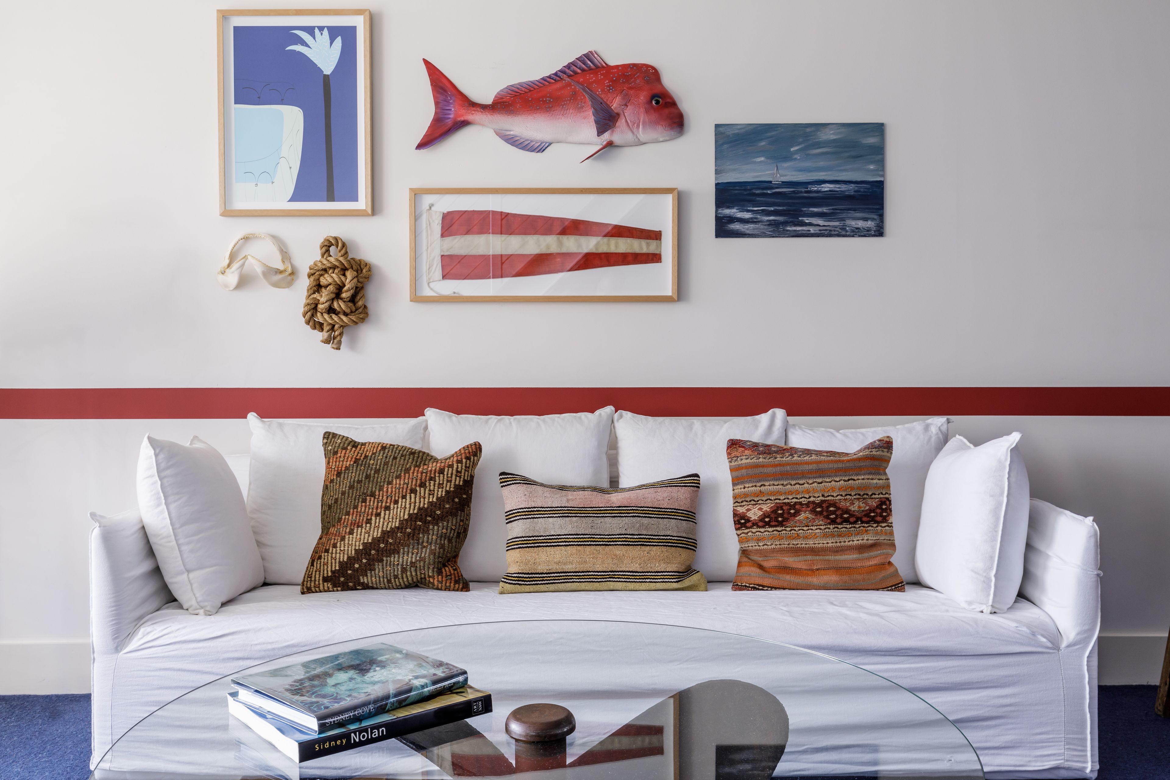 A white sofa with patterned cushions, a framed fish artwork, and a framed fish illustration on the wall.