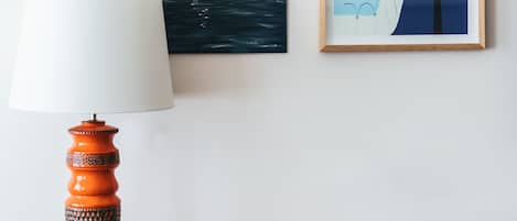 Una habitación con un escritorio de madera, una silla blanca, un cuadro con un barco y un cuadro con una ballena, además de una lámpara.