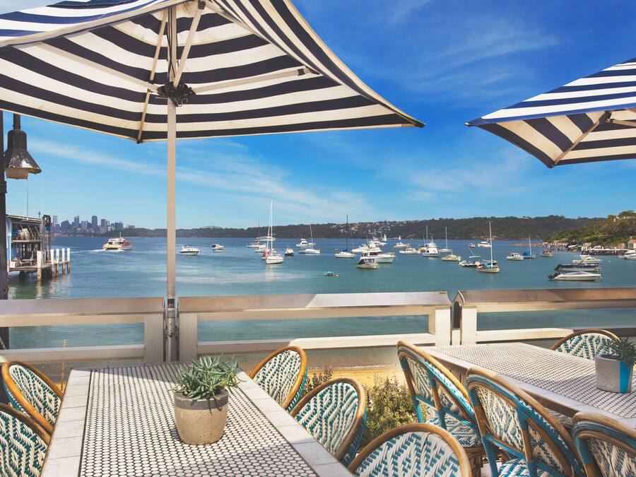 A seaside restaurant with striped umbrellas, a view of the marina, and wicker chairs.