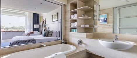 A modern bathroom with a large bathtub, a sink, and a mirror. There is a window with a view of the outside.