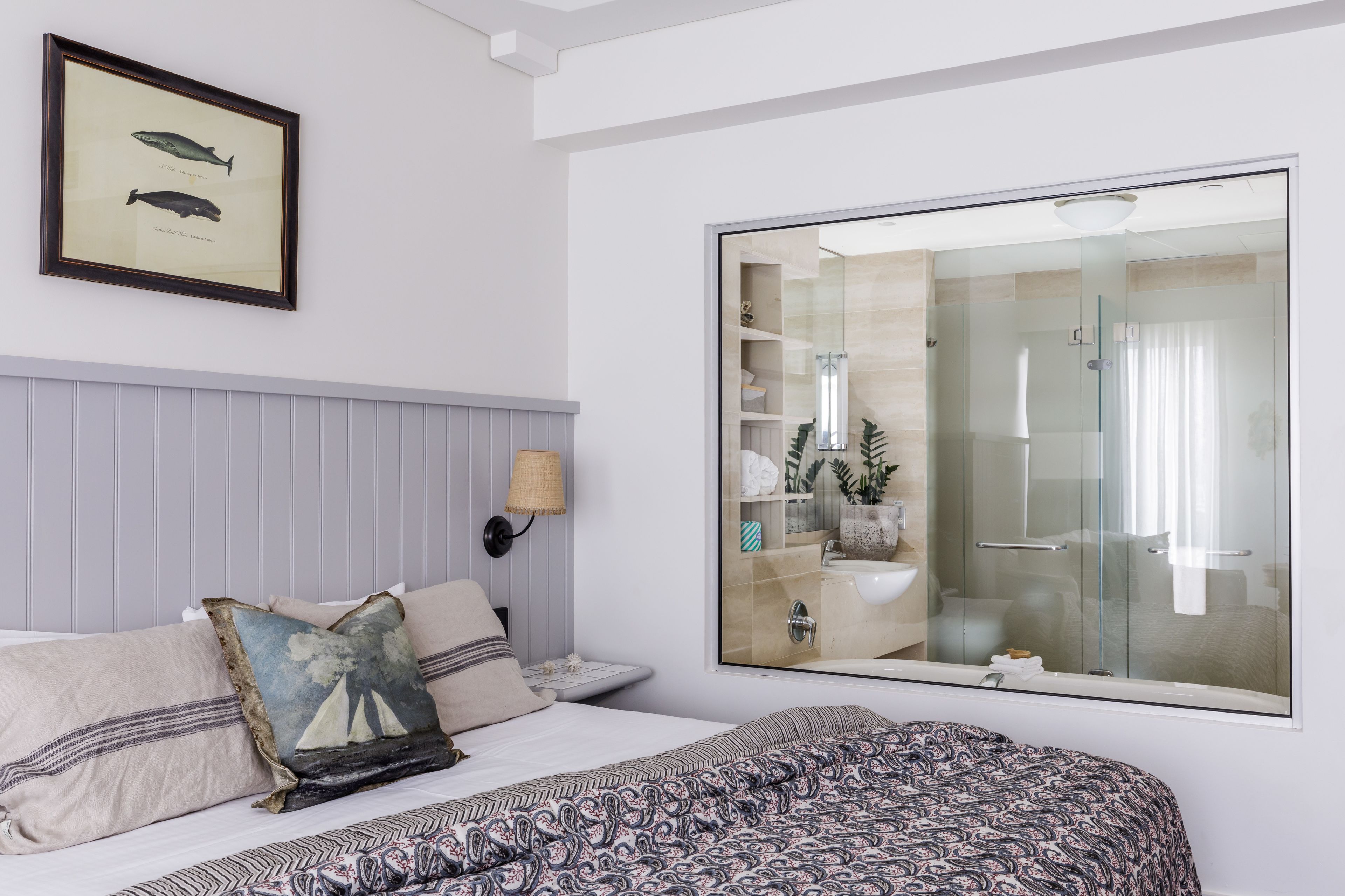 Habitación de hotel con cama, un espejo grande, un cuadro enmarcado de peces y un baño visible a través del espejo.