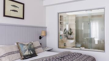 Habitación de hotel con cama, un espejo grande, un cuadro enmarcado de peces y un baño visible a través del espejo.