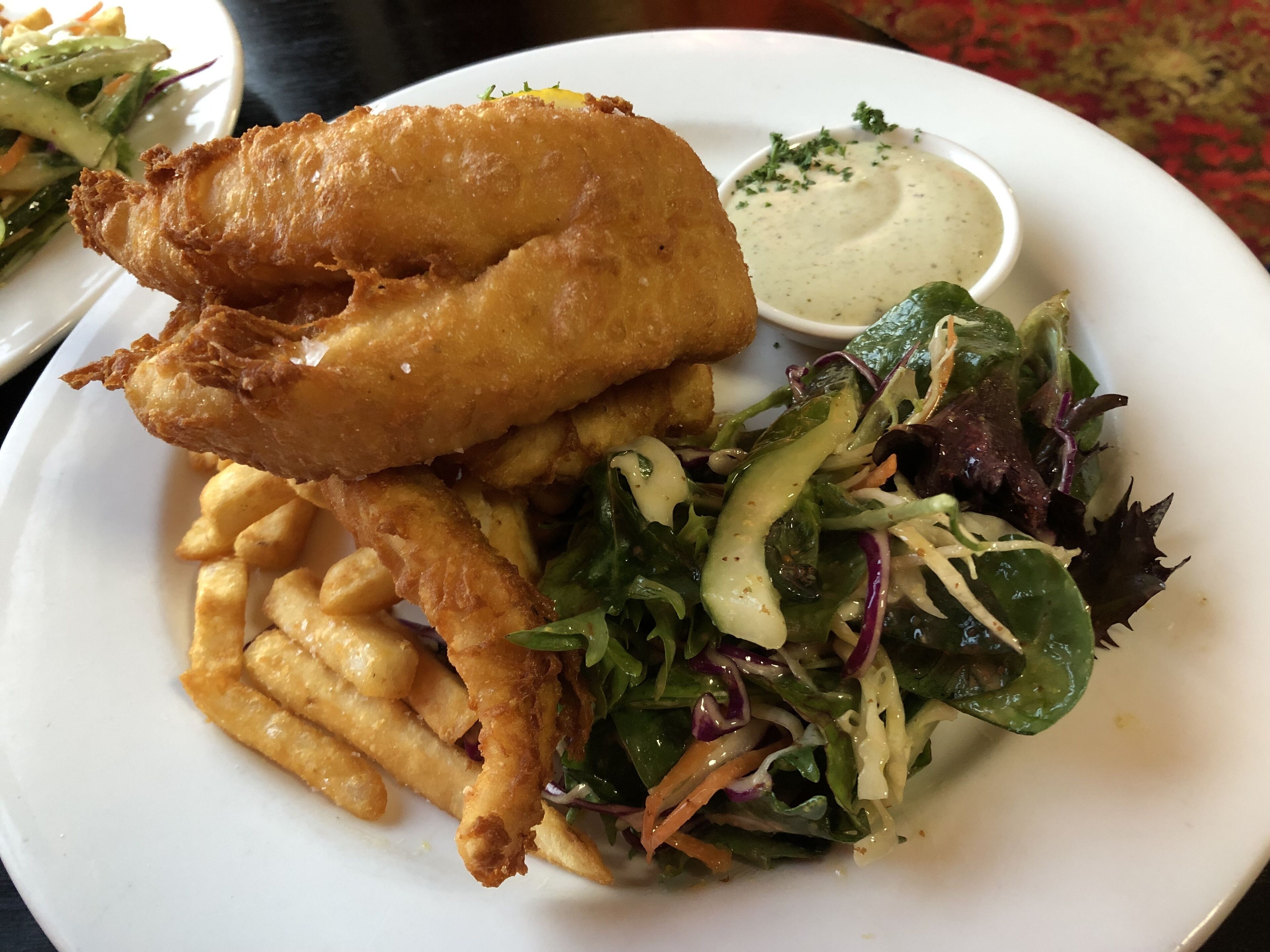 A plate of fish and chips with a side salad and dipping sauce.