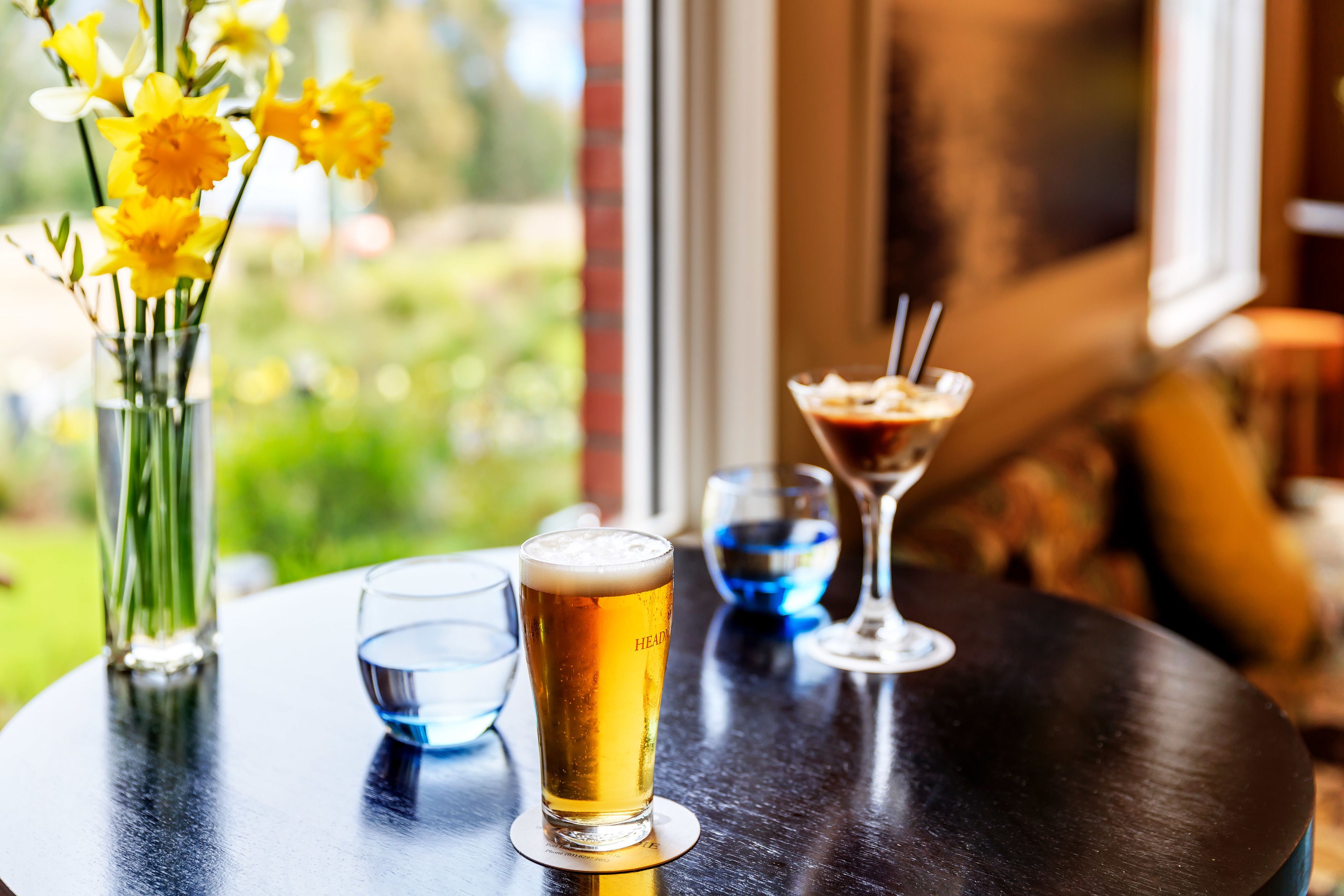 Una mesa con una jarra de cerveza, una copa de martini y un florero con flores amarillas.