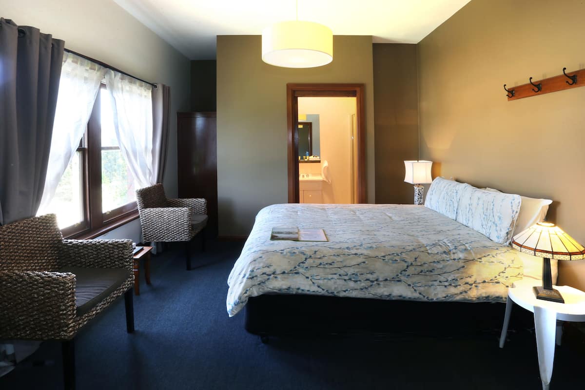 A hotel room with a bed, two chairs, a lamp, and a window with curtains.