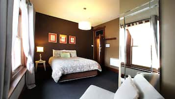 A hotel room with a bed, a bedside table with a lamp, a large mirror, and framed pictures on the wall.