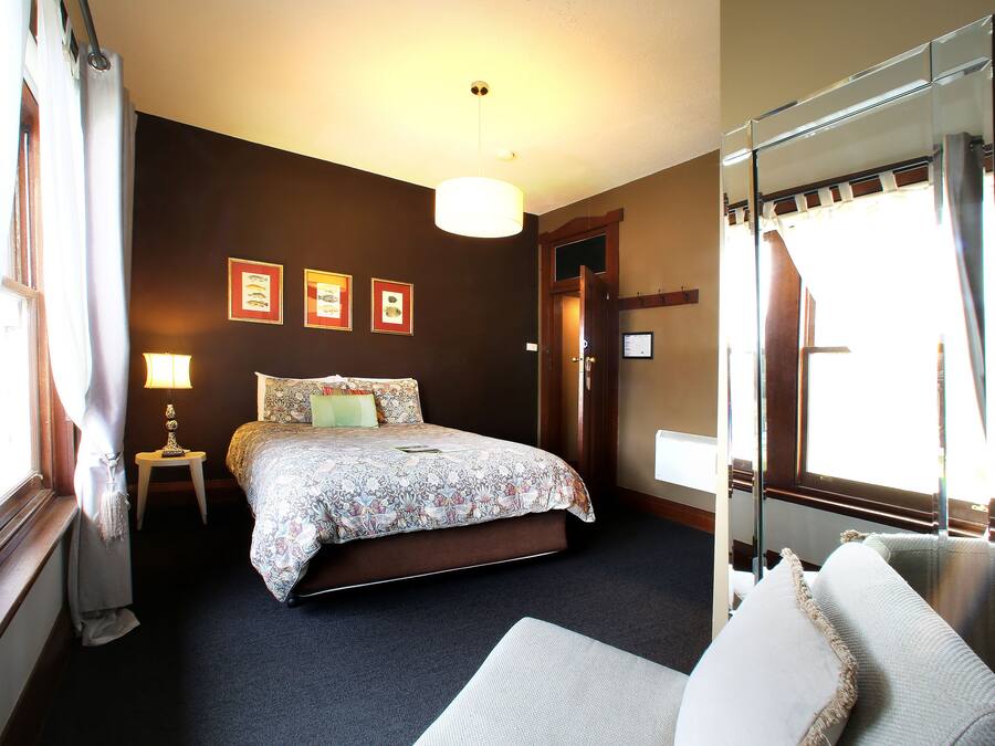 A hotel room with a bed, a bedside table with a lamp, a large mirror, and framed pictures on the wall.
