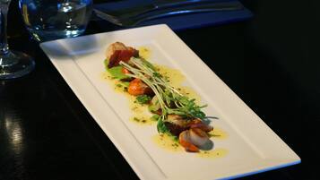 Un plato rectangular blanco con un plato de mariscos, adornado con hierbas y un chorrito de salsa, sobre una mesa oscura.