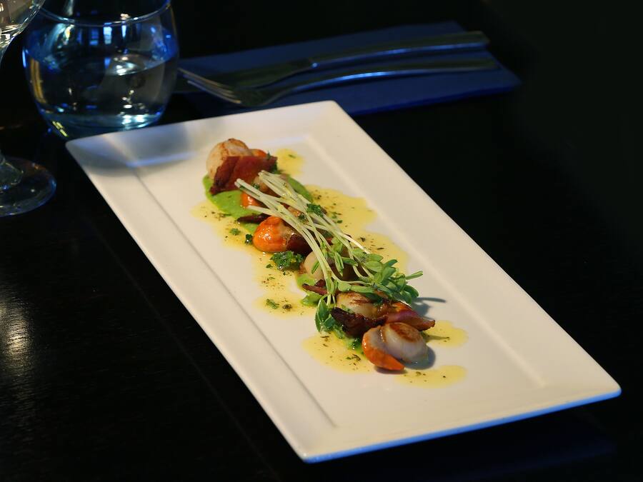 Un plato rectangular blanco con un plato de mariscos, adornado con hierbas y un chorrito de salsa, sobre una mesa oscura.