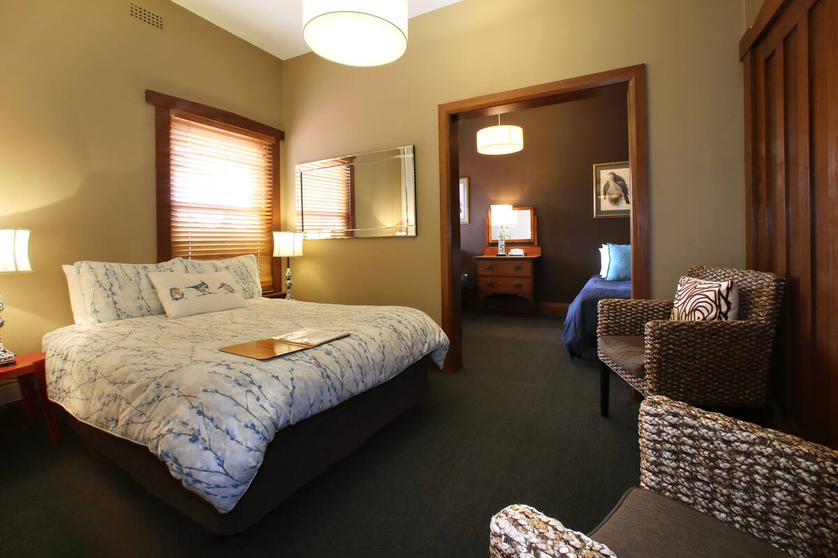 A hotel room with a large bed, a sitting area with a chair, a desk, and a mirror.