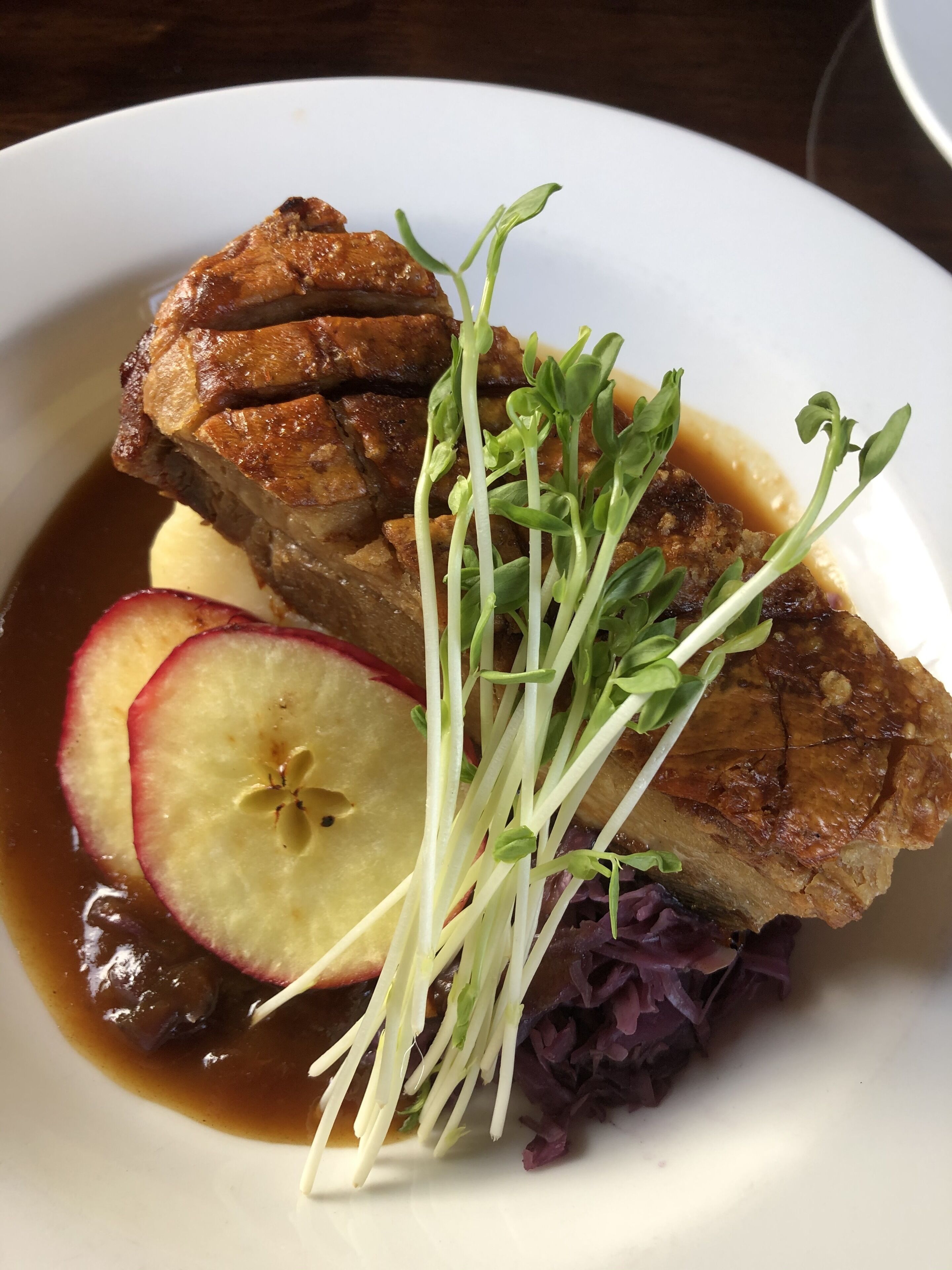Une assiette contenant un morceau de viande, des tranches de pomme, des jeunes pousses et une petite portion de chou rouge.
