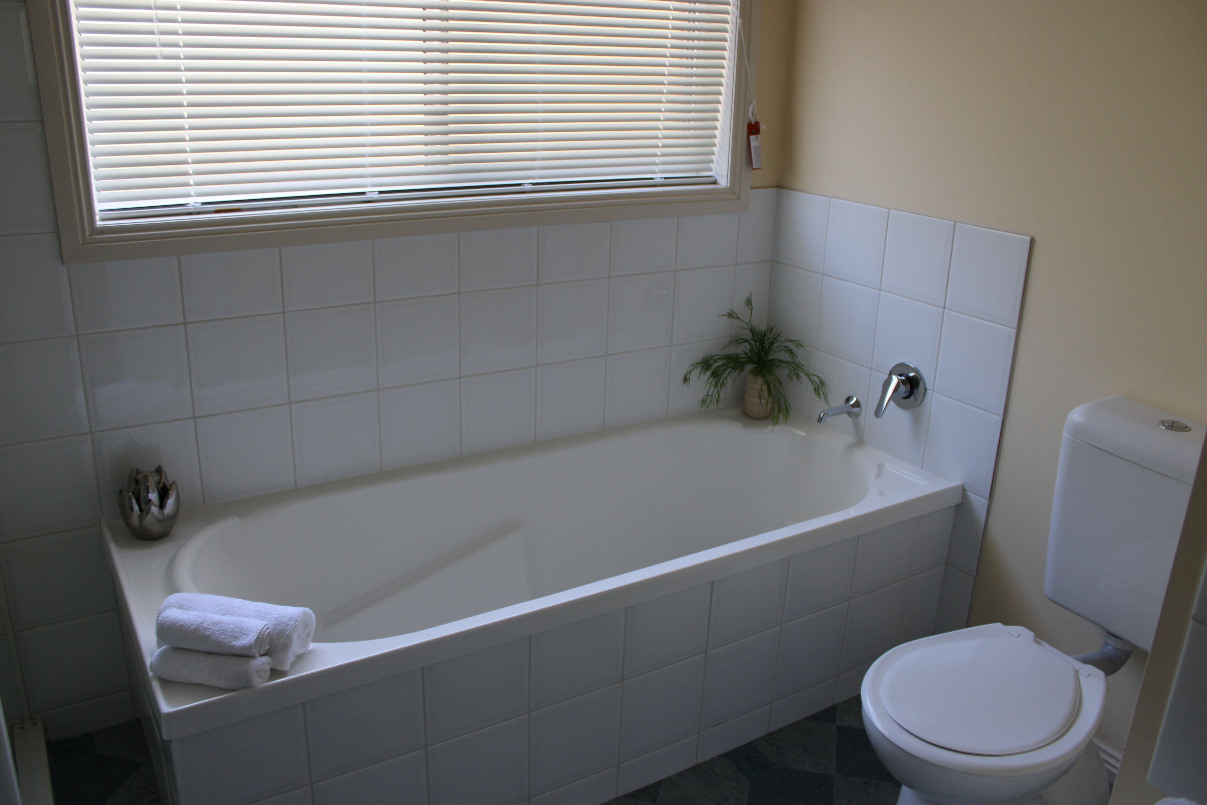 Un baño con una bañera blanca, un inodoro y una ventana con persianas.