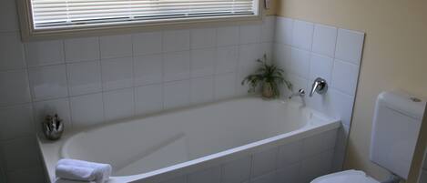 Un baño con una bañera blanca, un inodoro y una ventana con persianas.