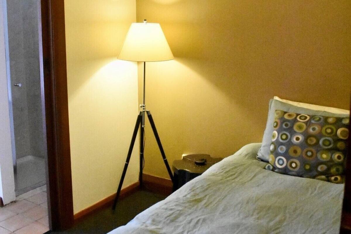 A hotel room with a bed, a floor lamp, and a door to a bathroom.