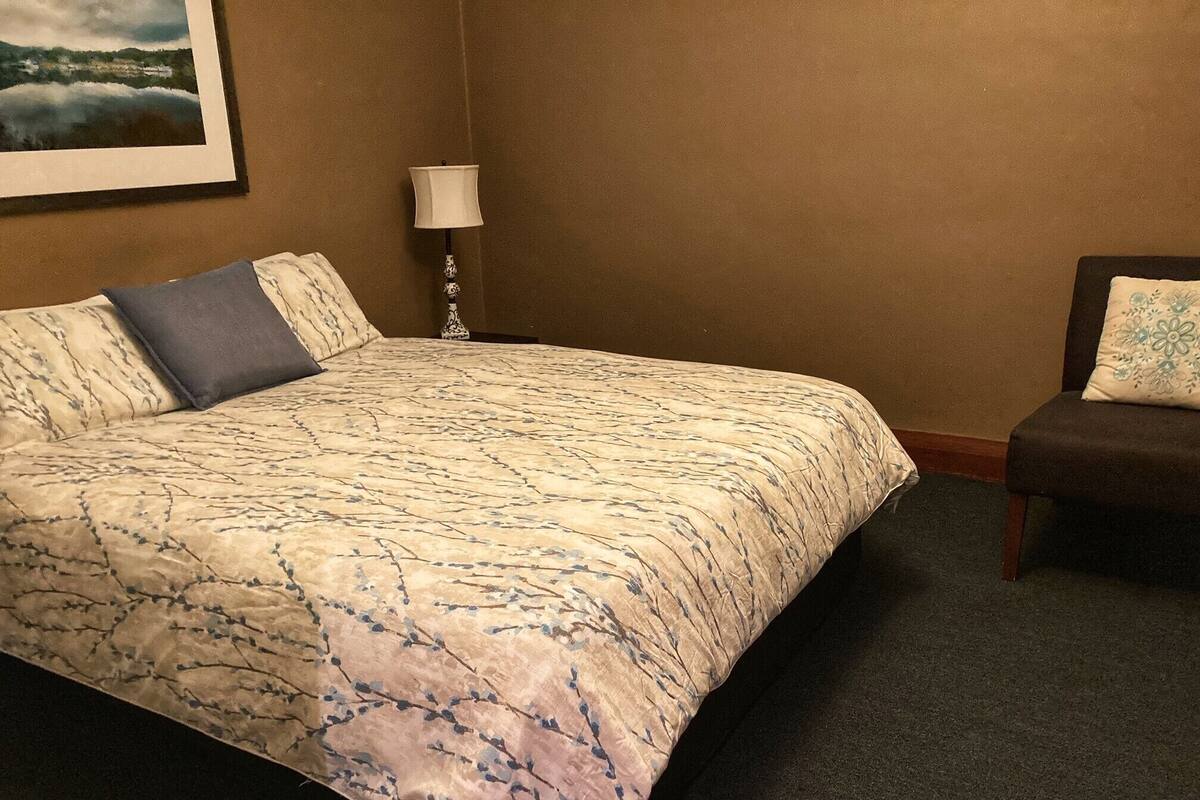 A hotel room with a bed, a nightstand, a lamp, and a chair.
