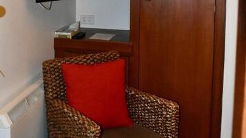 Um quarto pequeno com uma cadeira de vime, uma televisão fixada na parede e um guarda-roupa de madeira.