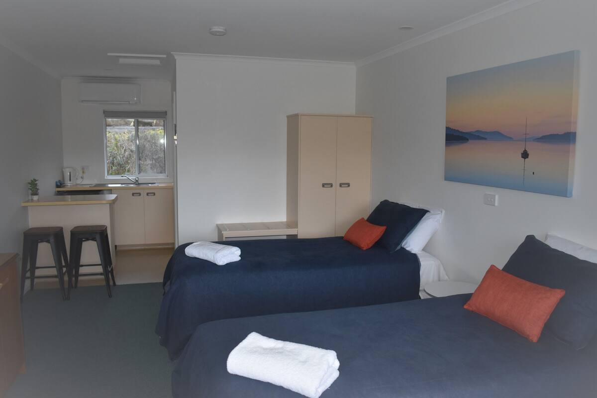 A hotel room with two beds, a desk, and a kitchenette.