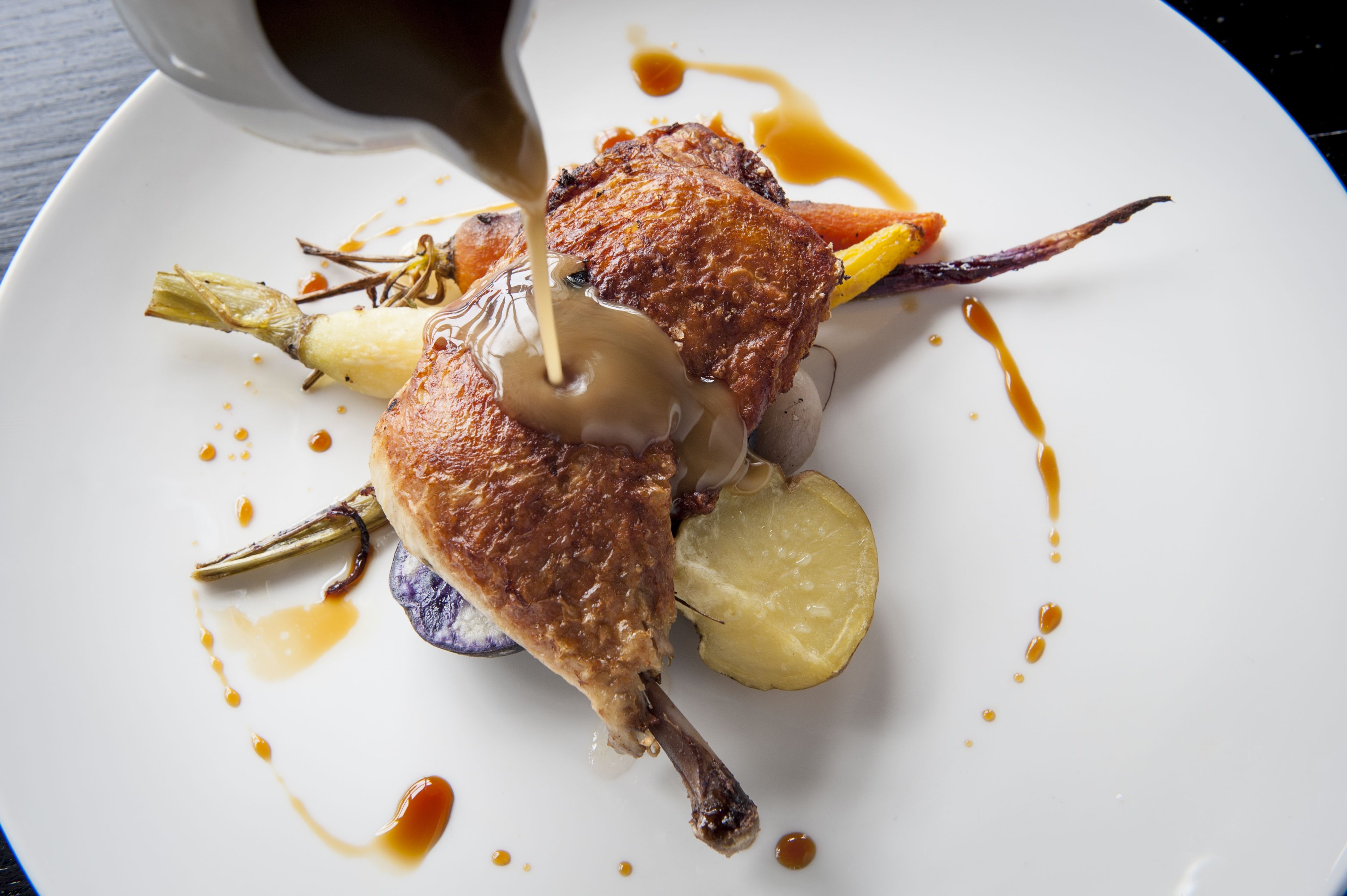 Een bord met geroosterde eend, aardappelen en saus.