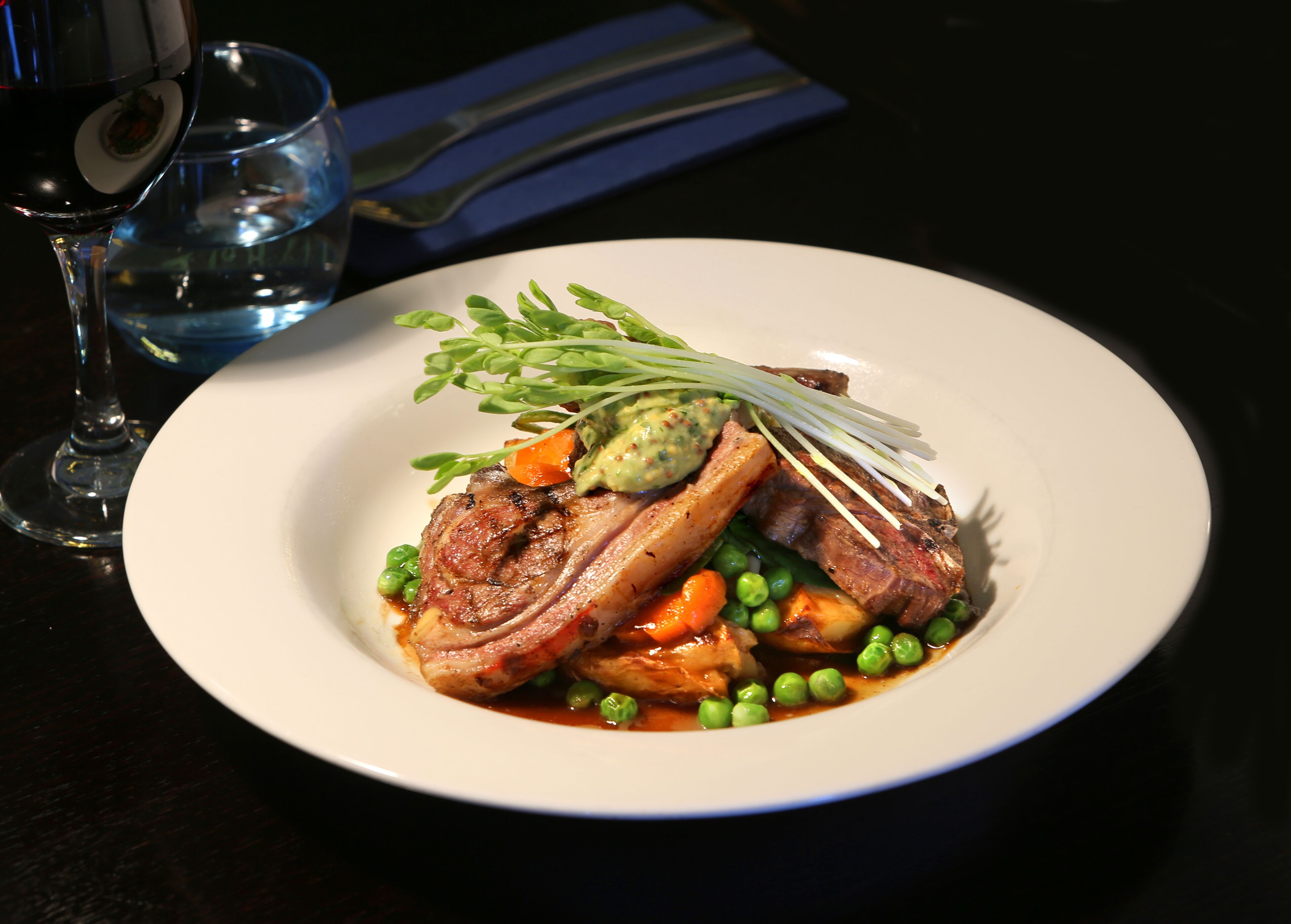 A plate of food with meat, peas, carrots, and a garnish on a white plate.