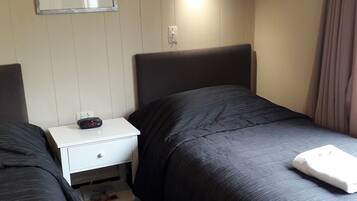 A hotel room with two beds, a nightstand with a clock, a small drawer, and a mirror on the wall.