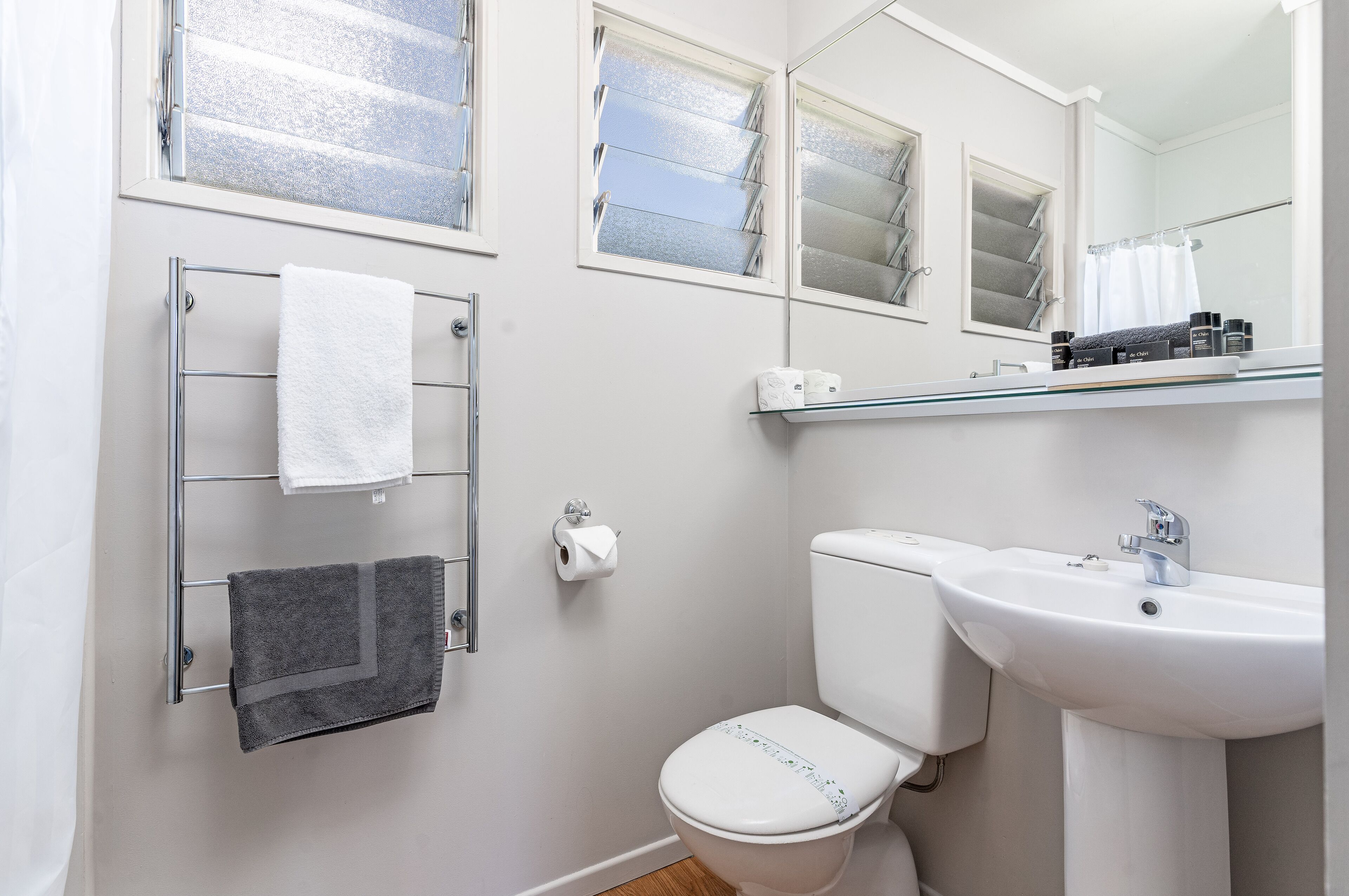 A bathroom with a toilet, sink, towel rack, and a window with blinds.