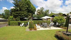 A patio area with outdoor seating, a small tree, and a hedge. - Amble Inn Motel - Masterton (Masterton)