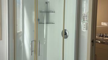 Ducha con cerramiento de vidrio, cabezal de ducha de mano y llave en la pared.