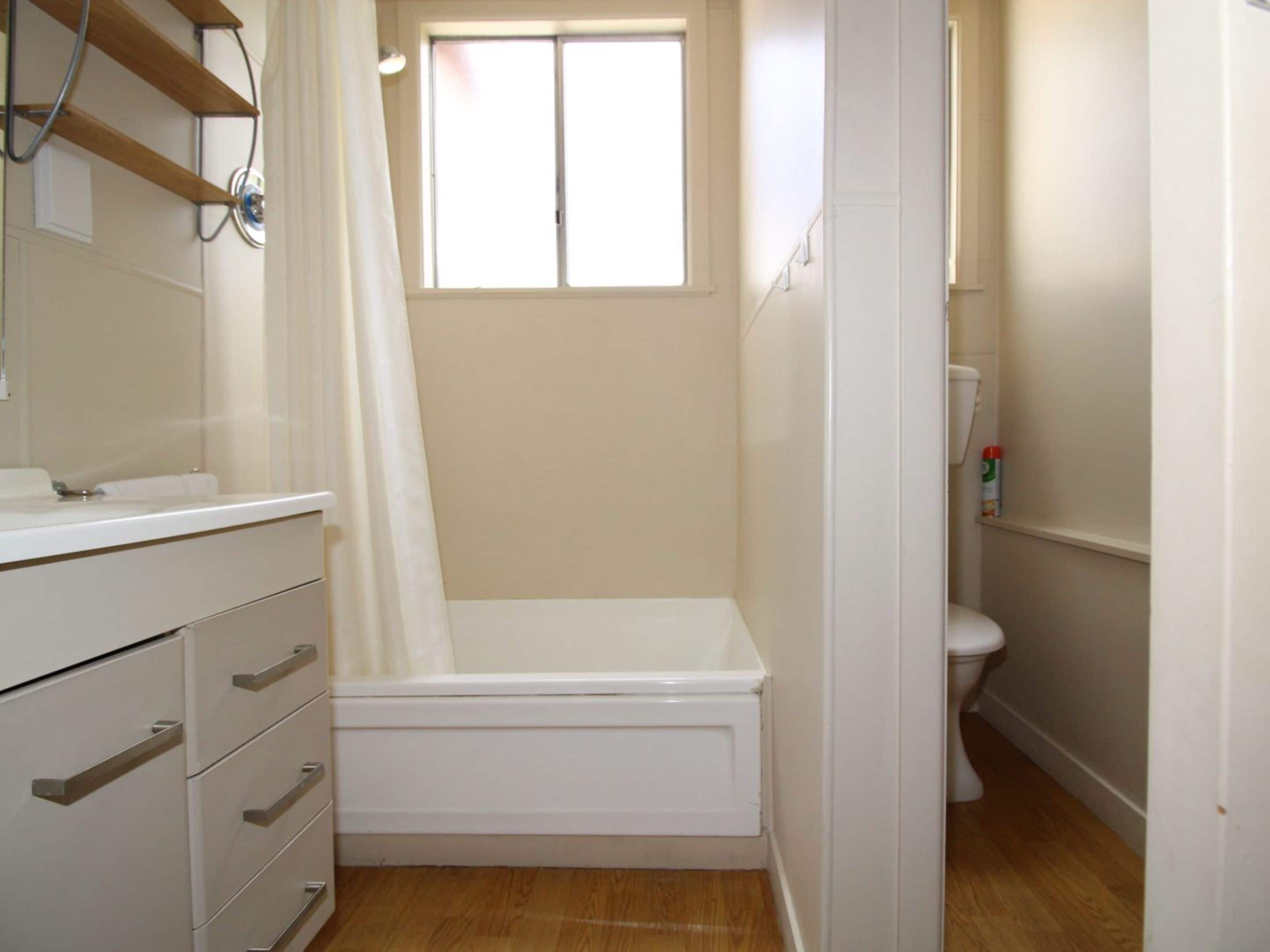 A small, clean bathroom with a shower, toilet, and a vanity with drawers.