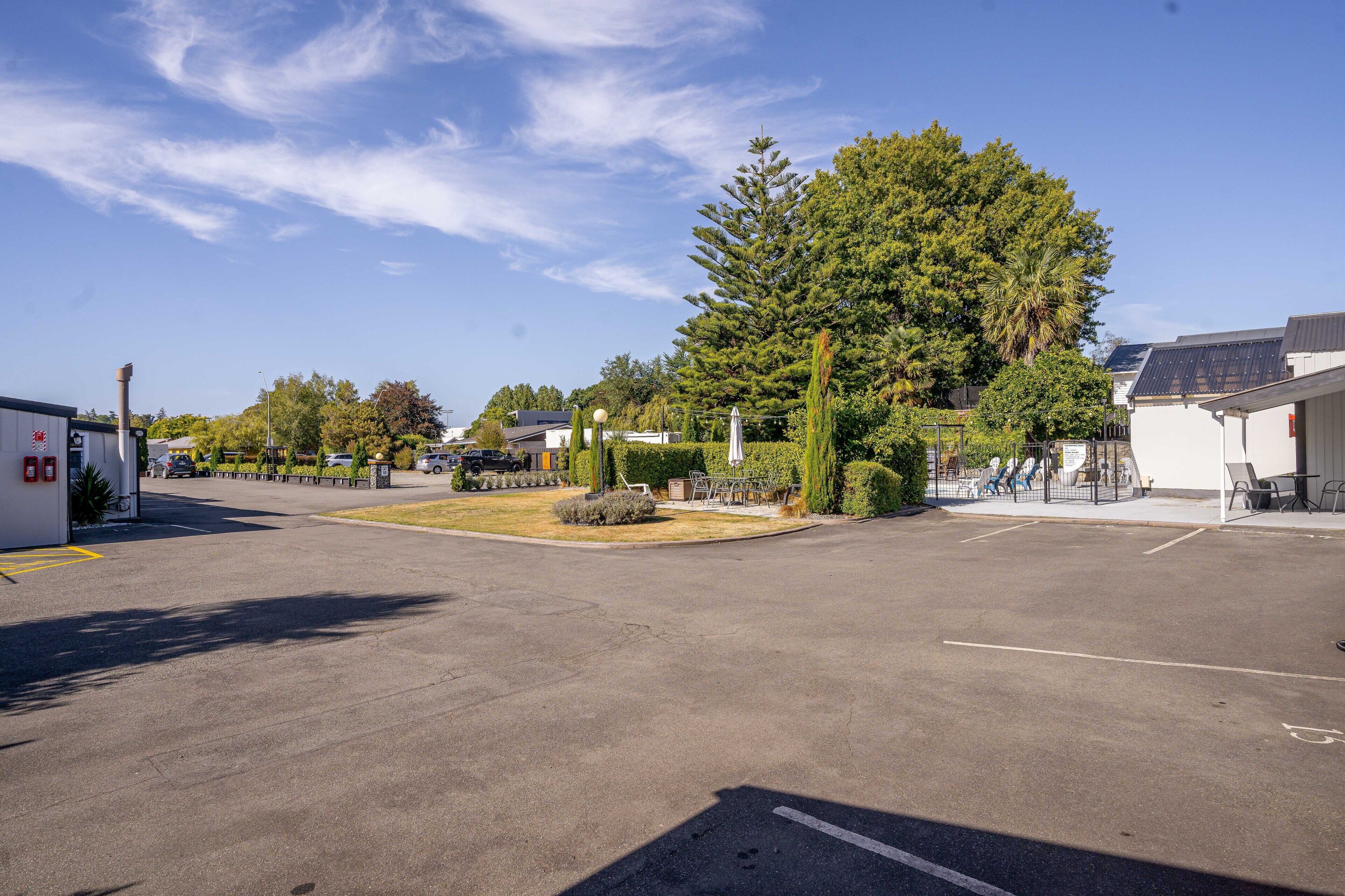 A parking lot with a building on the right, a large tree, and a clear sky.